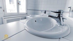 A modern bathroom with a white sink, chrome faucet, and a window providing natural light.