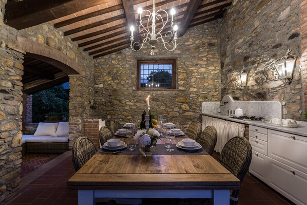 A stone-walled dining area with a wooden table set for a meal, a chandelier, and a window overlooking the outdoors.