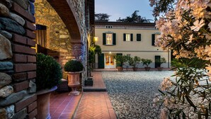 Un patio con un muro de piedra, un edificio con contraventanas y plantas en macetas.