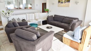 A modern living room with grey sofas, a white coffee table, and a wicker chair. - Individual villa with spectacular views of the ocean and the Algarve (ALFARROBEIRA)