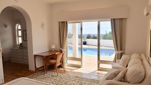 A bedroom with a bed, a desk, a chair, a sofa, and a view of a pool through a sliding glass door. - Individual villa with spectacular views of the ocean and the Algarve (ALFARROBEIRA)