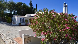 A building with a sign reading "Casa Penha de Santa Maria" in front of a white building with blue trim and a white lighthouse in the background. - Individual villa with spectacular views of the ocean and the Algarve (ALFARROBEIRA)