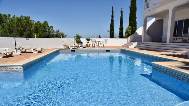 A swimming pool with lounge chairs and tables, a view of the sea, and a staircase leading to a covered area. - Individual villa with spectacular views of the ocean and the Algarve (ALFARROBEIRA)