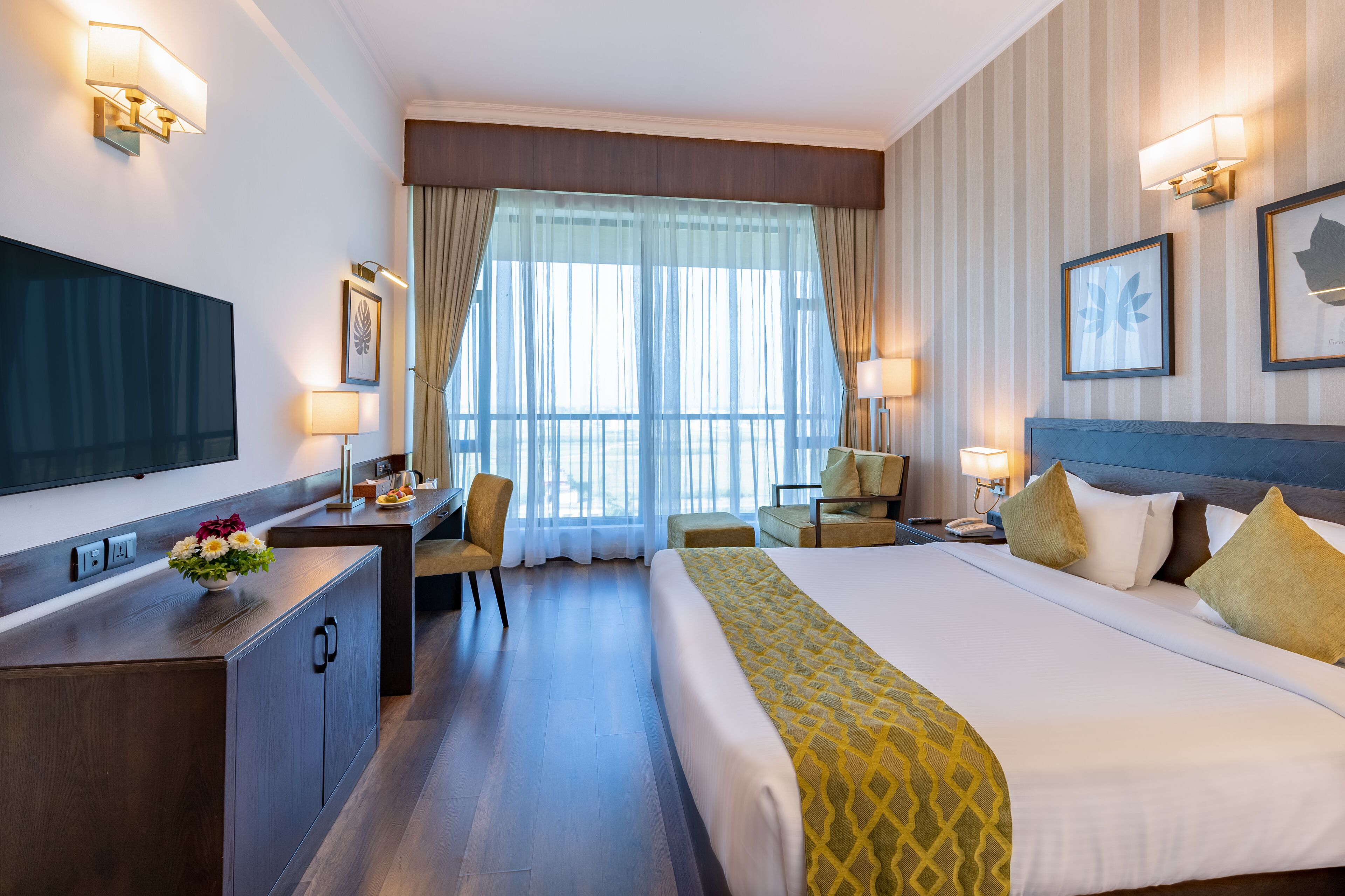 A hotel room with a large bed, a desk, a chair, a TV, and a window with curtains.