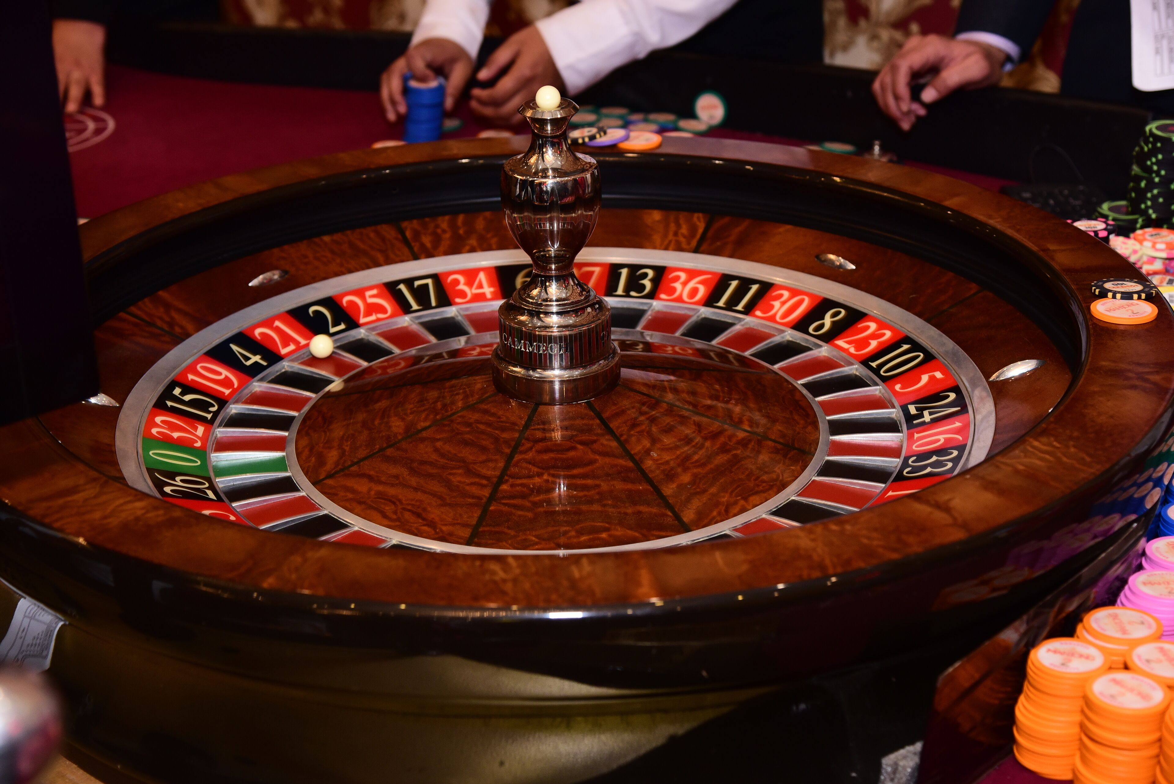 Ein Roulette-Rad mit rotierender Kugel, umgeben von Tischspielen und Spielchips.