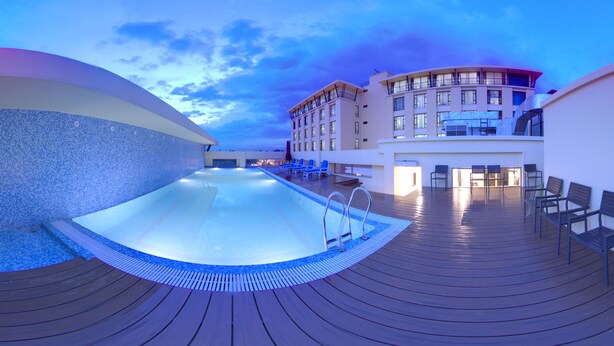 A rooftop pool area with a clear view of the sky, a pool with a blue edge, and a seating area with chairs. - Soaltee Westend Premier (Nepalgunj)