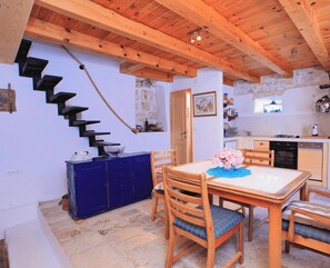Un coin repas avec une table et des chaises en bois, un buffet bleu et un mur en pierre.