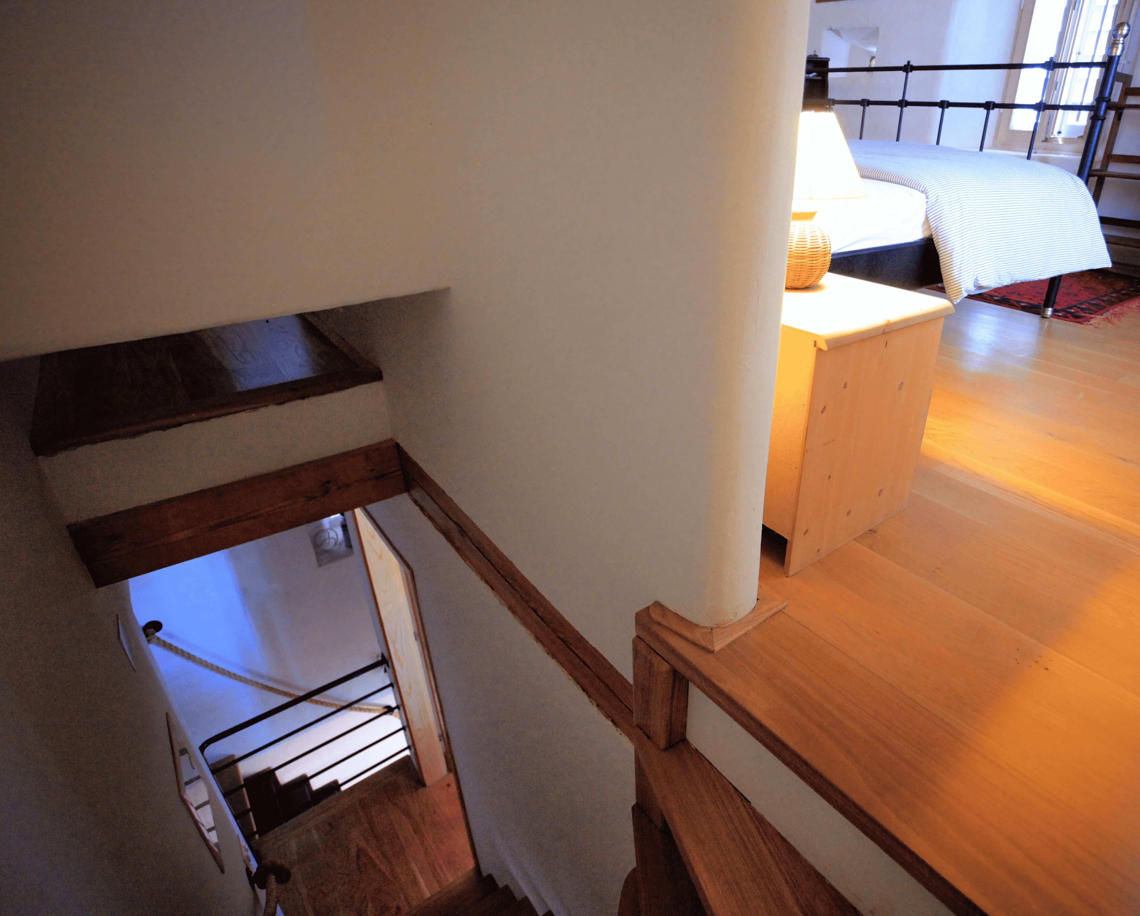 A staircase with wooden railings leading to a bedroom with a bed and a chair.