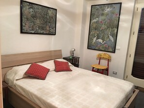 A bedroom with a wooden bed, two red pillows, a nightstand with a lamp, and two large paintings on the walls. - Villa with heated pool (Castelbuono (Pa))