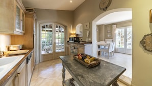 A kitchen with a marble countertop, a fruit basket on a table, and a dining area with a table and chairs. - Villa La Lavande Has A Heated Pool And Magnificent Sea, Golf And Mountain Views (Châteauneuf-Grasse)