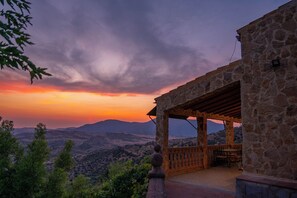 Un edificio de piedra con un porche cubierto y vistas a un paisaje montañoso.