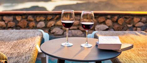 Two wine glasses on a table with a book beside them, overlooking a scenic view of mountains and a body of water.