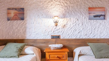 Una habitación con dos camas, una mesita de noche de madera, una lámpara de pared y dos cuadros enmarcados.