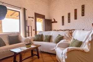Une pièce chaleureuse avec un canapé blanc, une table en bois et une porte donnant sur l’extérieur.