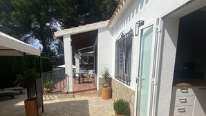 Un patio exterior cubierto con suelo de piedra, un pérgola y plantas en macetas.