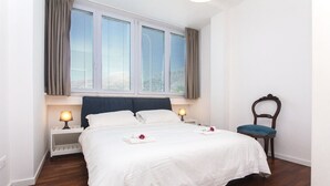 A neatly made bed with white linens, a wooden nightstand with a lamp, a chair, and a window with blinds. - Modern detached villa near the beach of Mondello (Palermo)