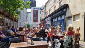 An outdoor seating area with tables and chairs, surrounded by buildings with various storefronts.