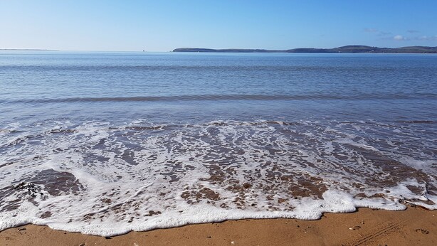 A beach with gentle waves, clear skies, and distant landforms.