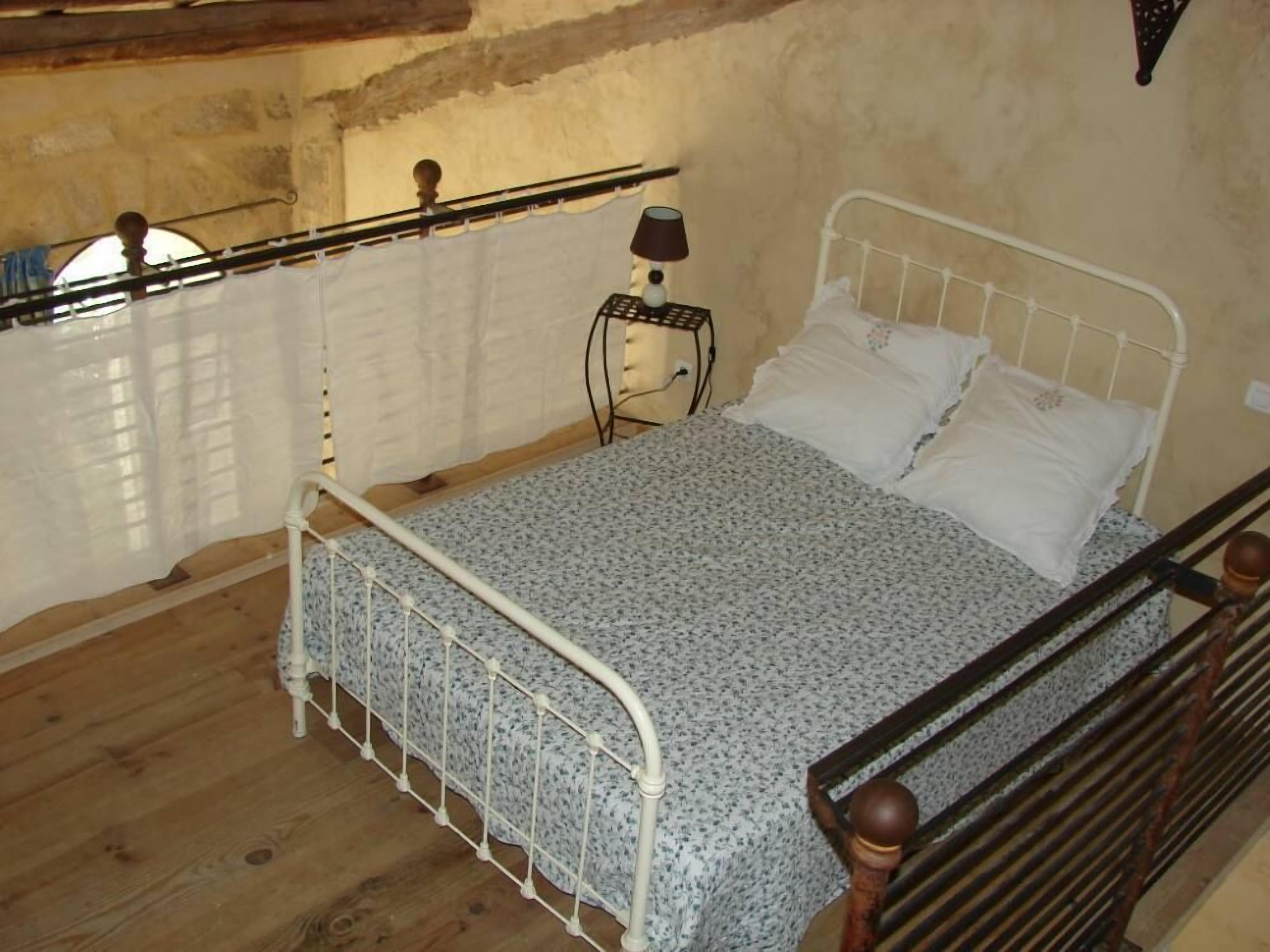 Une chambre à coucher avec un lit, une table de chevet, une lampe et une fenêtre avec un rideau.