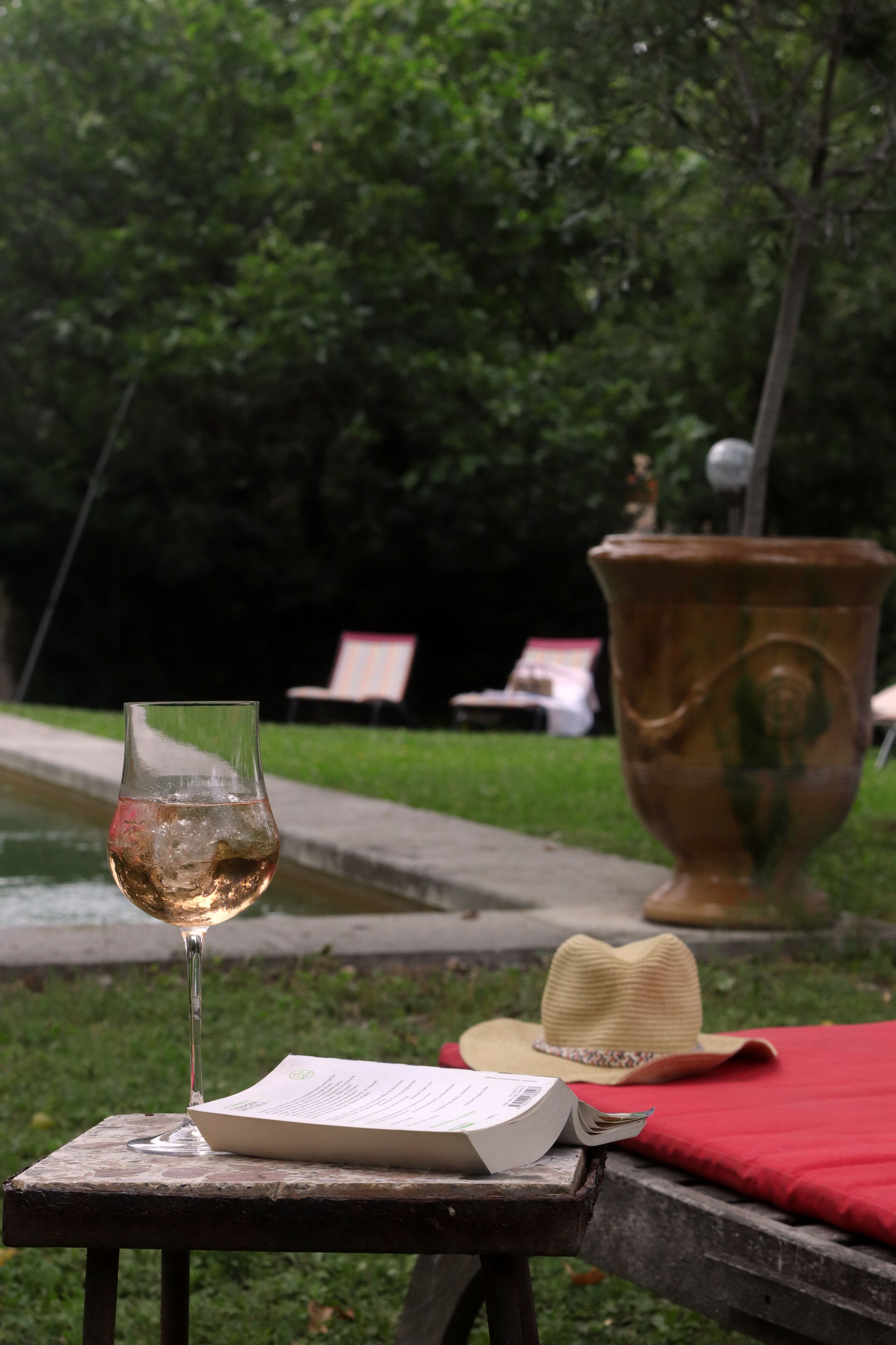 A glass of wine on a table with a menu, a hat, and a red cloth.