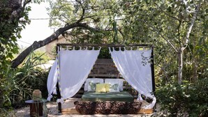 Una cama con doseles blancos, colchón verde y almohadas decorativas en un jardín.