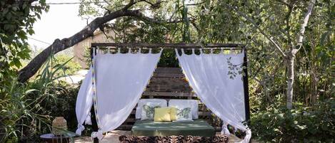 A bed with white canopies, a green mattress, and decorative pillows in a garden setting.