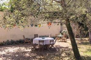 Un'area pranzo all'aperto con un tavolo rotondo e sedie, circondata da alberi e da un muro.