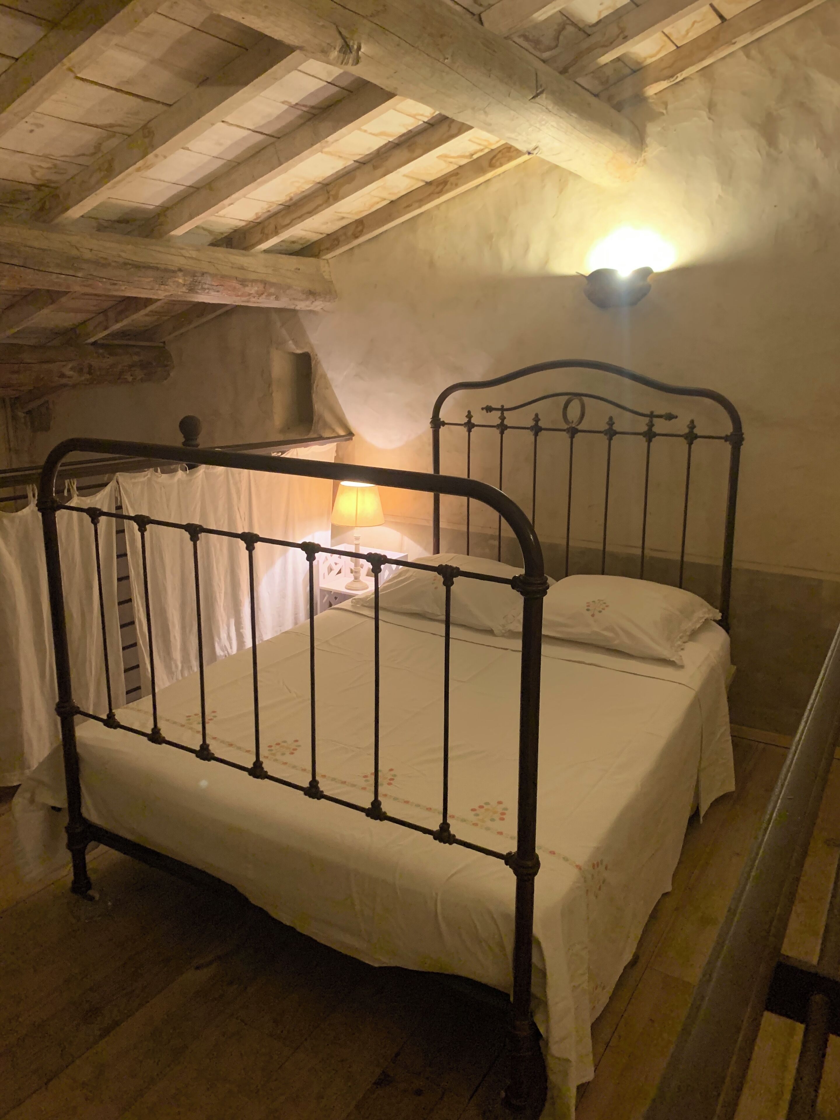 Een rustieke slaapkamer met een houten plafond, een metalen bedframe en een enkele bedlamp.