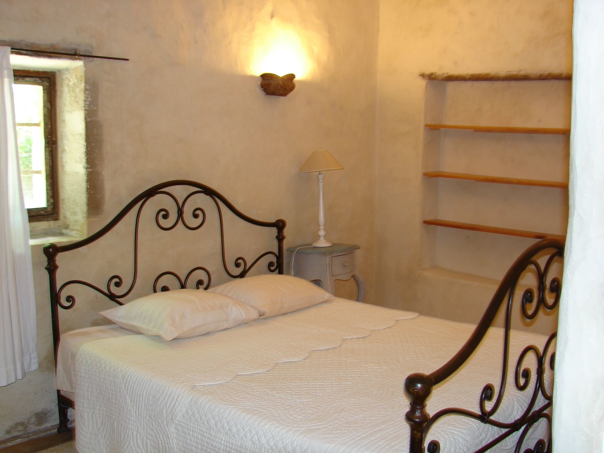 A bedroom with a bed, a nightstand, a wall-mounted lamp, and a window.
