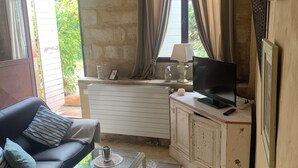 Una sala de estar acogedora con un sofá negro, una mesa de centro de vidrio, un televisor sobre un mueble bajo y un amplio ventanal con cortinas.