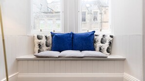 A white window seat with a bench, two blue cushions, and patterned pillows.