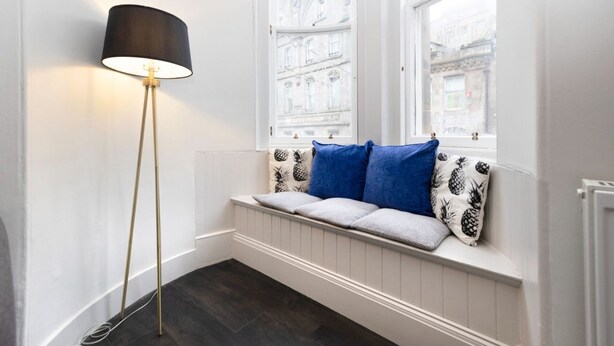 A room with a window seat, a floor lamp, and a view of buildings outside.