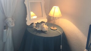 A small round table with a lamp and a decorative shell, a mirror, and a white curtain.