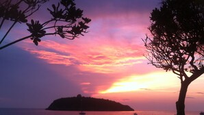 A sunset view with silhouettes of a tree and a distant island.