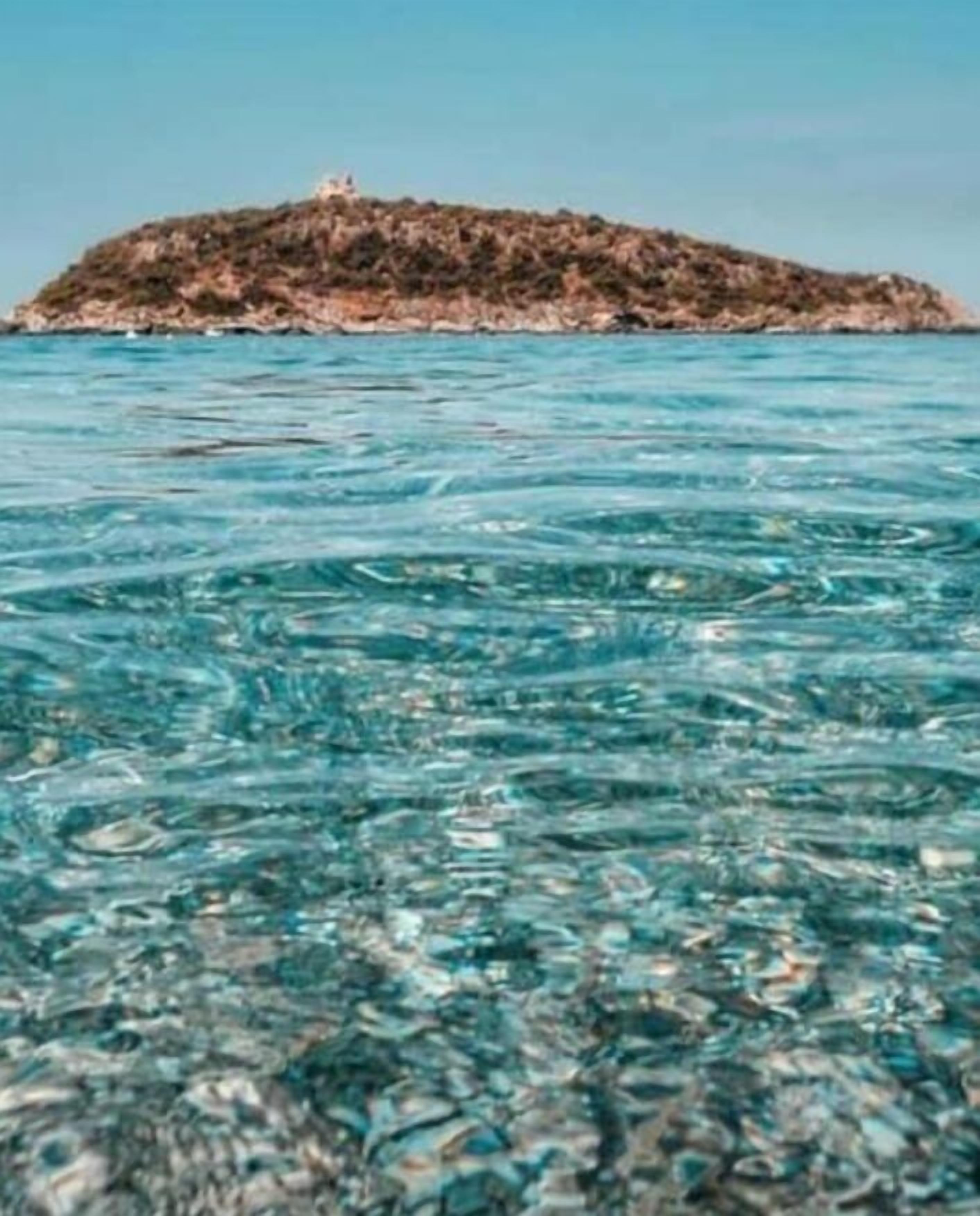 A clear view of a small island with rocky terrain and a few structures on top.