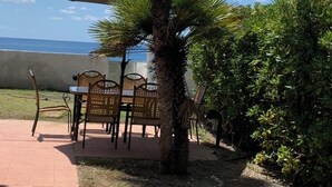 A patio with a table and chairs, a palm tree, and a view of the sea.
