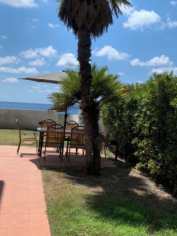 A patio with a table and chairs, a palm tree, and a view of the sea.