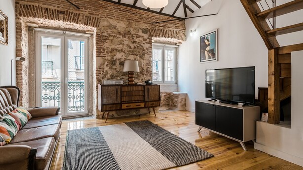Un soggiorno con pavimento in legno, un divano, una TV, una lampada e una parete in mattoni.
