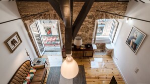 Una camera in stile loft con travi a vista in legno, un divano in pelle, un lampadario e vista sulla strada attraverso una porta in vetro.