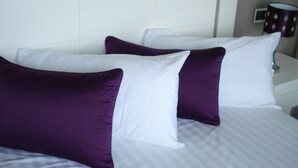 A bed with white and purple pillows, a white headboard, and a nightstand with a lamp. - Whim Apartment. Front line beach, 2 bedrooms, 2 bath, Spa. Wifi. English TV (Fuengirola)