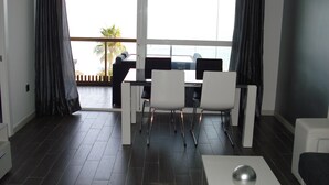 A modern living room with a dining area, dark wooden flooring, and large windows offering a view of palm trees. - Whim Apartment. Front line beach, 2 bedrooms, 2 bath, Spa. Wifi. English TV (Fuengirola)