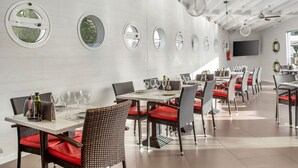 Un comedor moderno con espejos redondos en la pared, techo blanco y sillas con acolchado rojo.