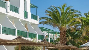 Un edificio blanco con barandillas verdes y una palmera en primer plano.