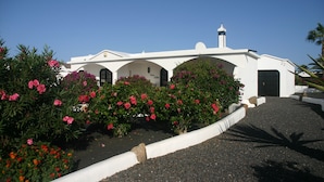 Un bâtiment blanc, doté d’un dôme et de fenêtres en arc de cercle, entouré de fleurs roses et de verdure.