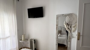 Habitación de hotel con cama, televisor de pantalla plana, radiador, una mesita con jarrón y un espejo grande.