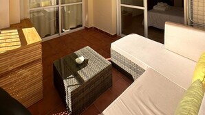 Habitación de hotel con cama, una mesita, un sofá, un banco de madera y una puerta corrediza de vidrio.