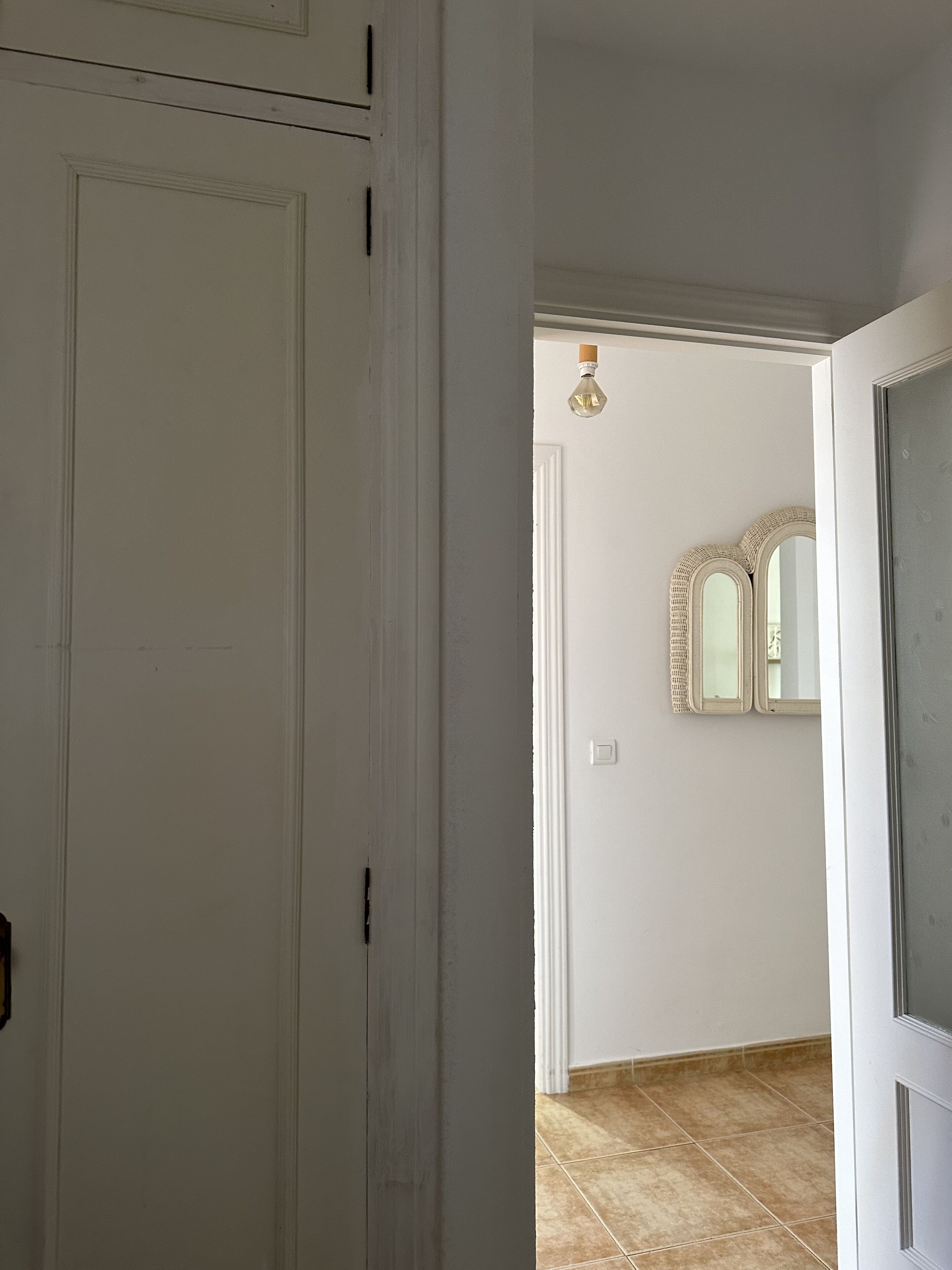 Um corredor com uma porta branca, uma luminária e um espelho na parede.