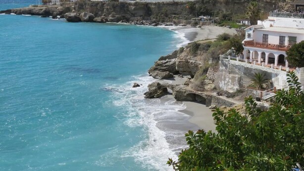 Un hotel costero con varias edificaciones blancas, una costa rocosa y una playa.
