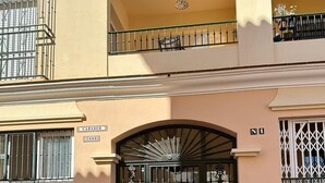 Un edificio con entrada protegida por un portón, plantas en macetas y un balcón con barandilla.