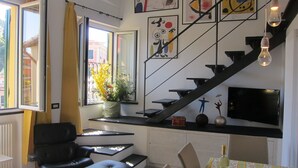 A modern living room with a black leather sofa, a dining table with chairs, a staircase with a TV, and artwork on the walls. - Architectural designed  central apartment a few steps from the beaches. PARKING. (sestri levante)